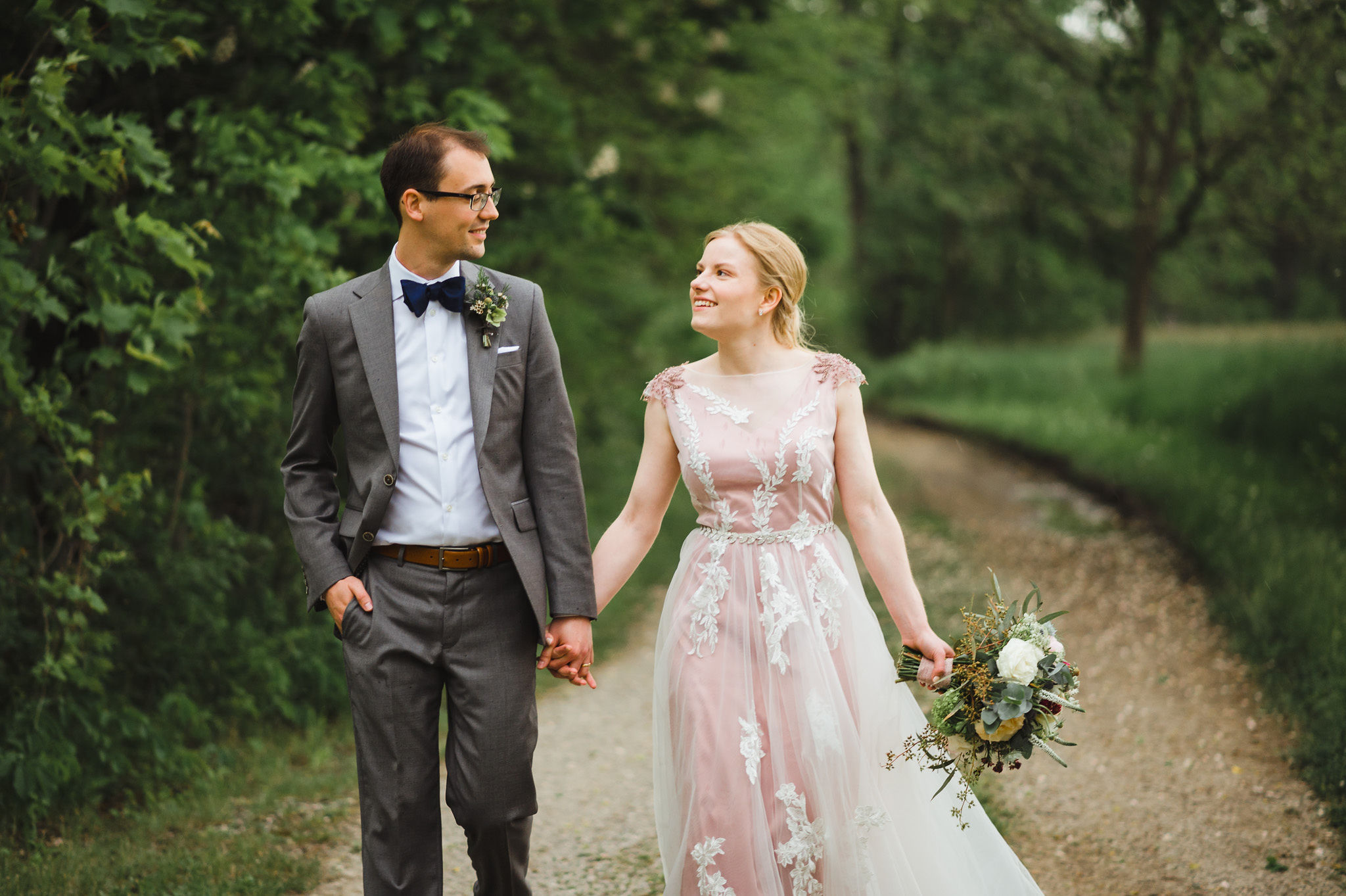 bride and groom holding hands as they walk along a forested path during their charming southern style wedding at Ruthven National Historic Site near Hamilton