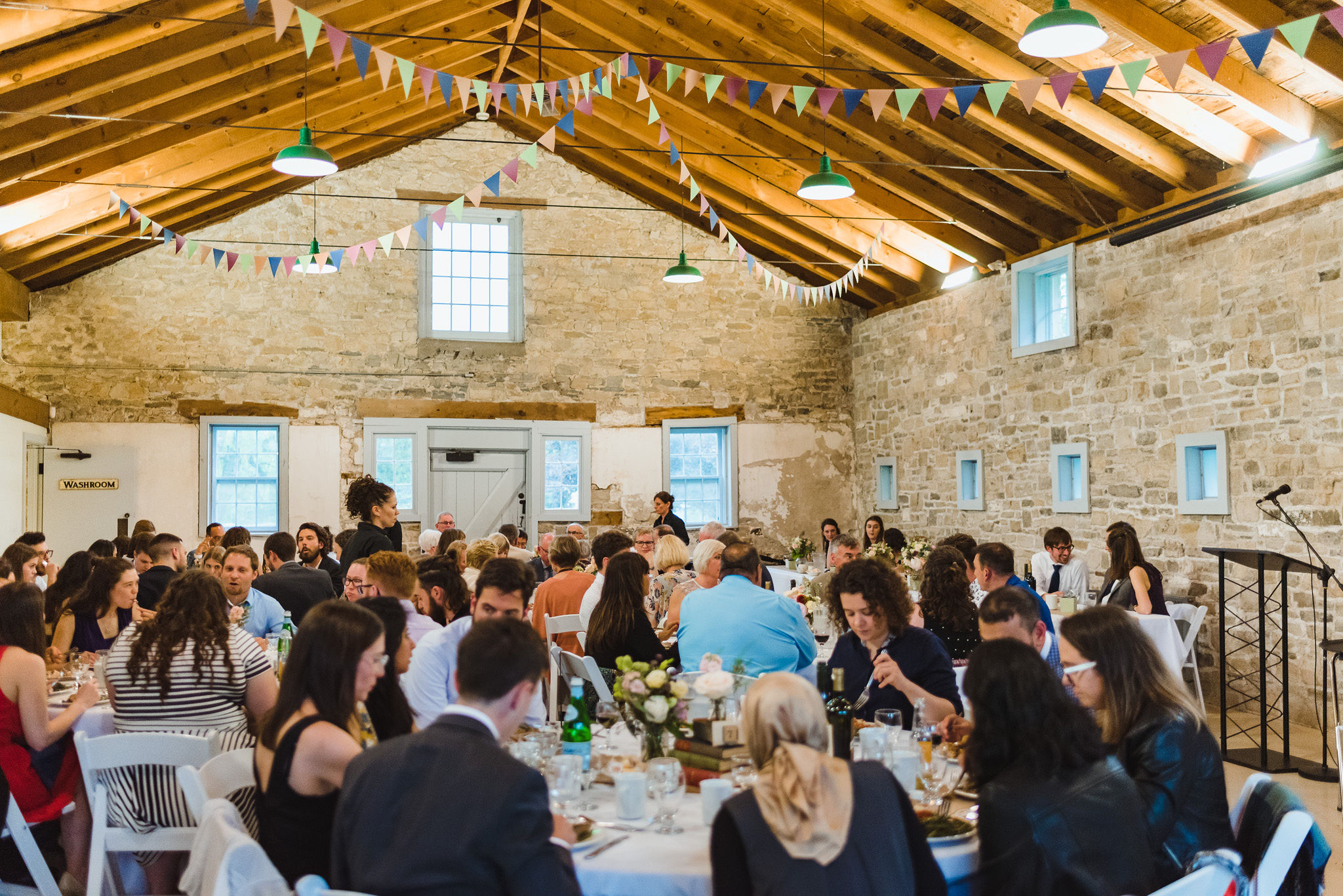 tables filled with wedding guests inside large stone reception hall during a charming southern style wedding at Ruthven National Historic Site near Hamilton