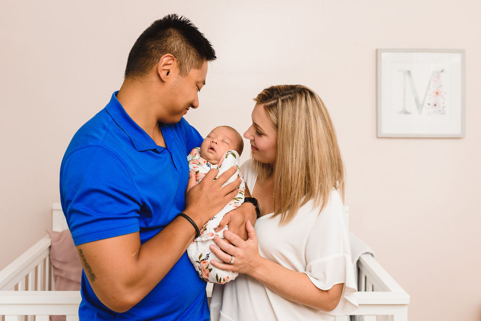 A father and a mother holding their swaddled newborn between them and looking on affectionately Toronto family photography
