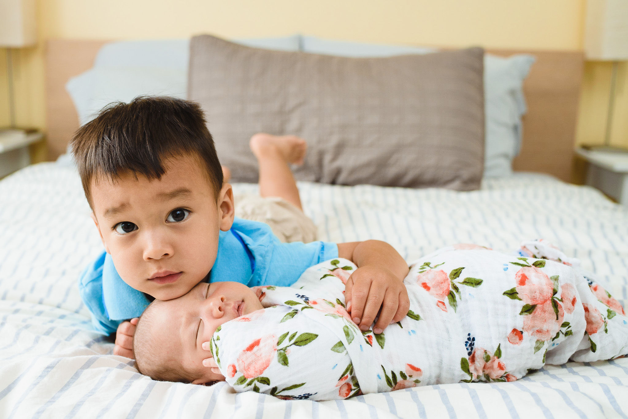 toddler crouching down to hug his newborn sibling that's swaddled in a floral blanket Toronto family photography