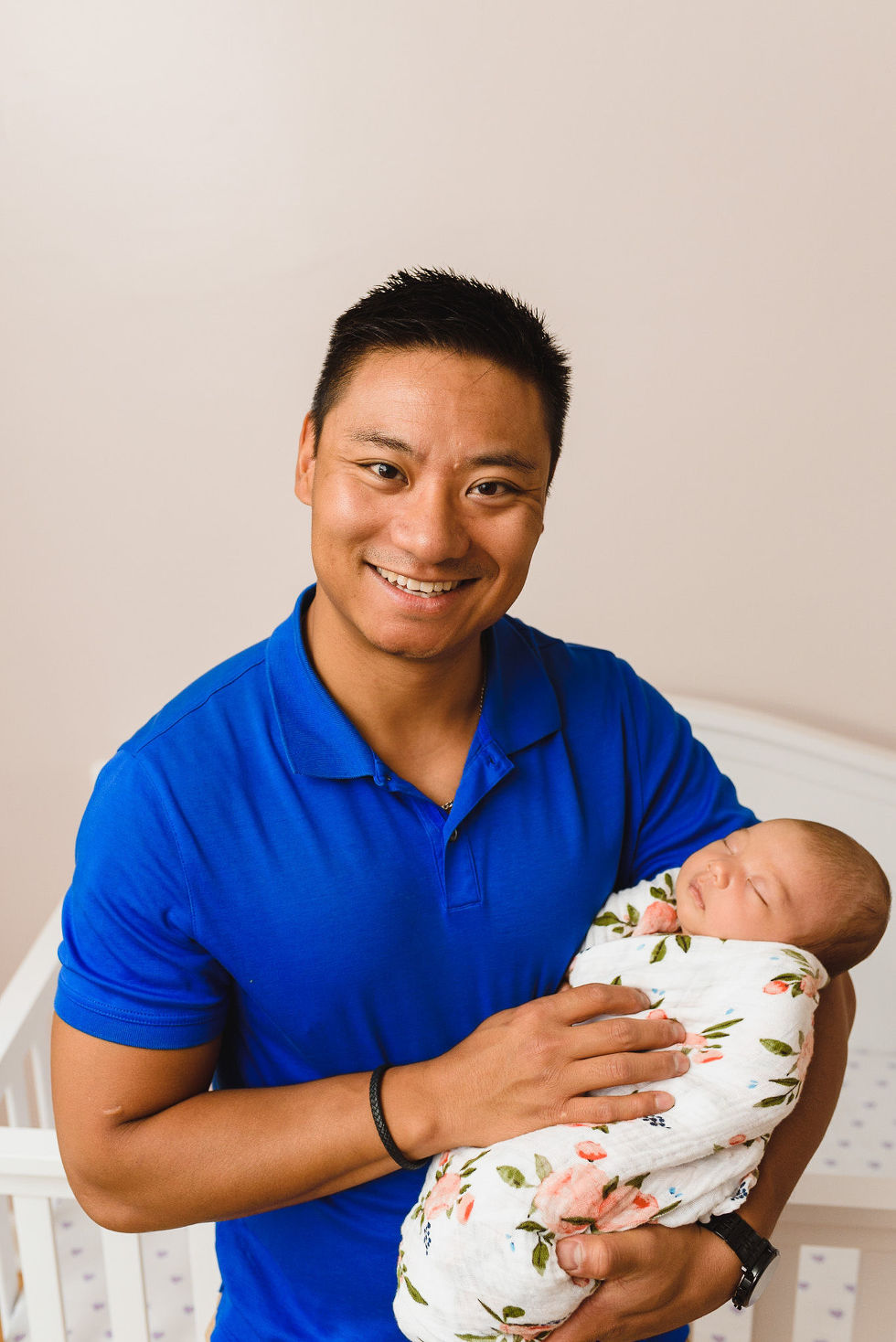 father smiling as he sits on his bed holding his newborn in a floral swaddle Toronto family photography 