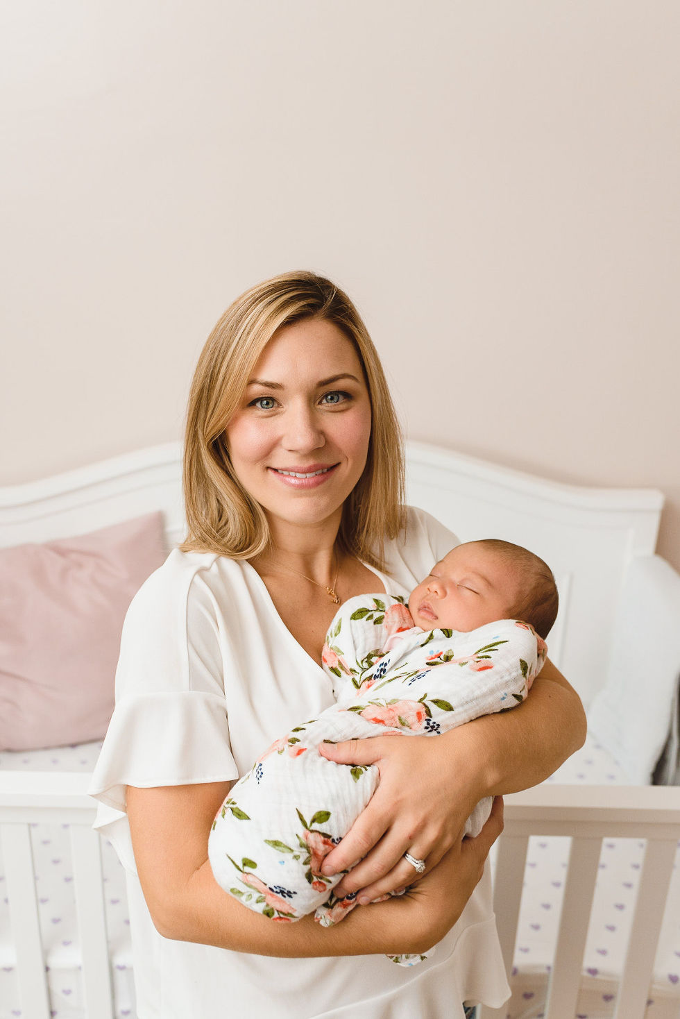 mother smiling as she sits on her bed holding her newborn in a floral swaddle Toronto family photography 