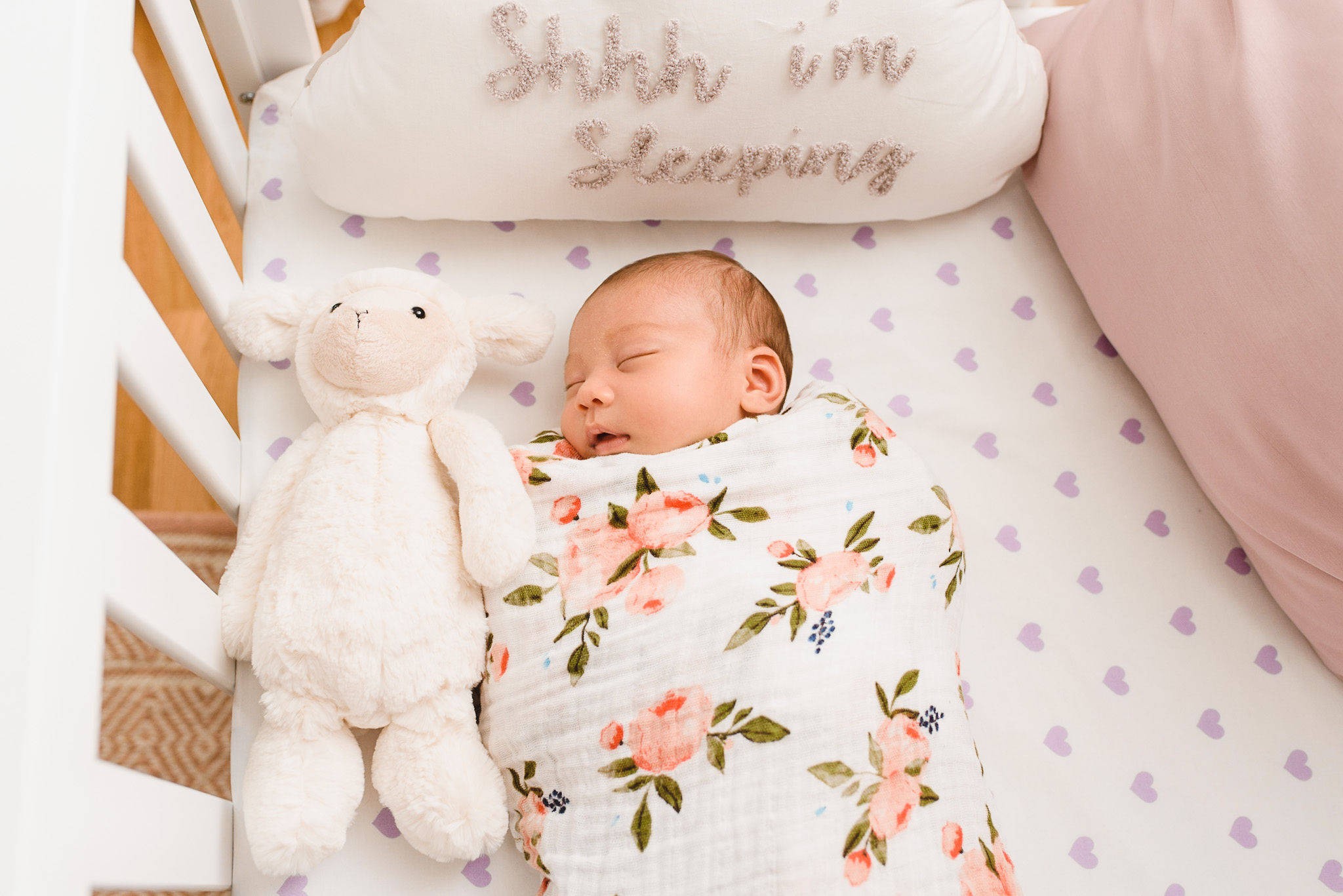 A baby swaddled in a floral blanket and sleeping in a crib with stuffed bunny and a pillow that says shhh i'm sleeping Toronto family photography