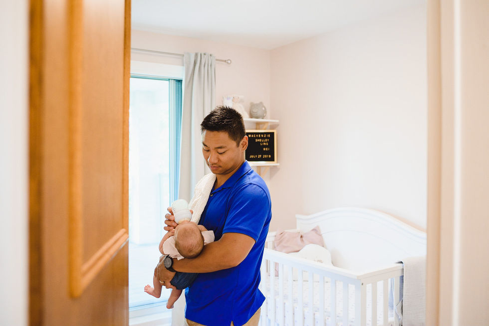 A father standing in the nursery room holding his baby as he feeds it a bottle Toronto family photography